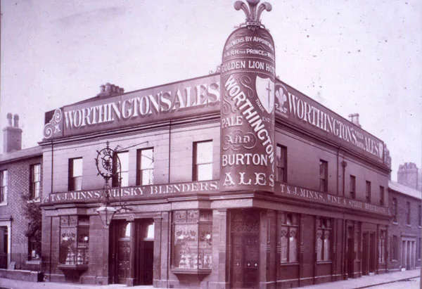 Old sepia photograph of a corner pub covered in painted lettering for Worthington's Ales and Burton Ales, a tall decorated corner panel naming the Golden Lion Hotel and a fascia for T and J Minns, wine and spirit merchants