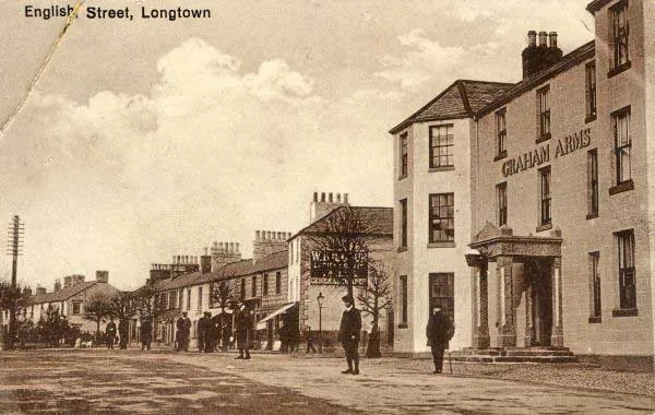Old sepia postcard of a wide village street with men standing in the road, and on the right a tall three-storey stone hotel with Graham Arms lettered across it and a columned porch, captioned English Street, Longtown