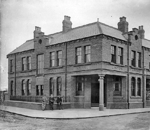 Old photograph of a large two-storey brick corner hotel with a canted corner entrance on a stone column and the words Linton Holme Hotel along the fascia, three men in suits and caps standing by the railings