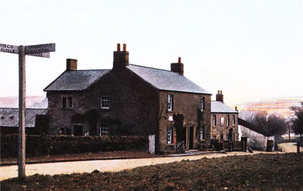 Old tinted postcard of a two-storey stone inn behind a hedge at a road junction, with a wooden fingerpost pointing to Carlisle, Brisco and Broadfield, and a bicycle leaning by the door
